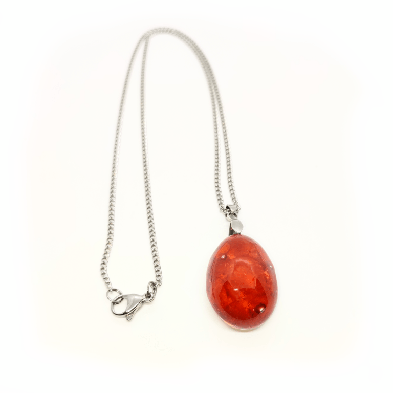 Ein orangefarbener Orgonit Anhänger mit den Edelsteinen Karneol, Orangencalcit & Herkimer Diamant. Die Panzerkette des Schmuckstückes ist silberfarben.