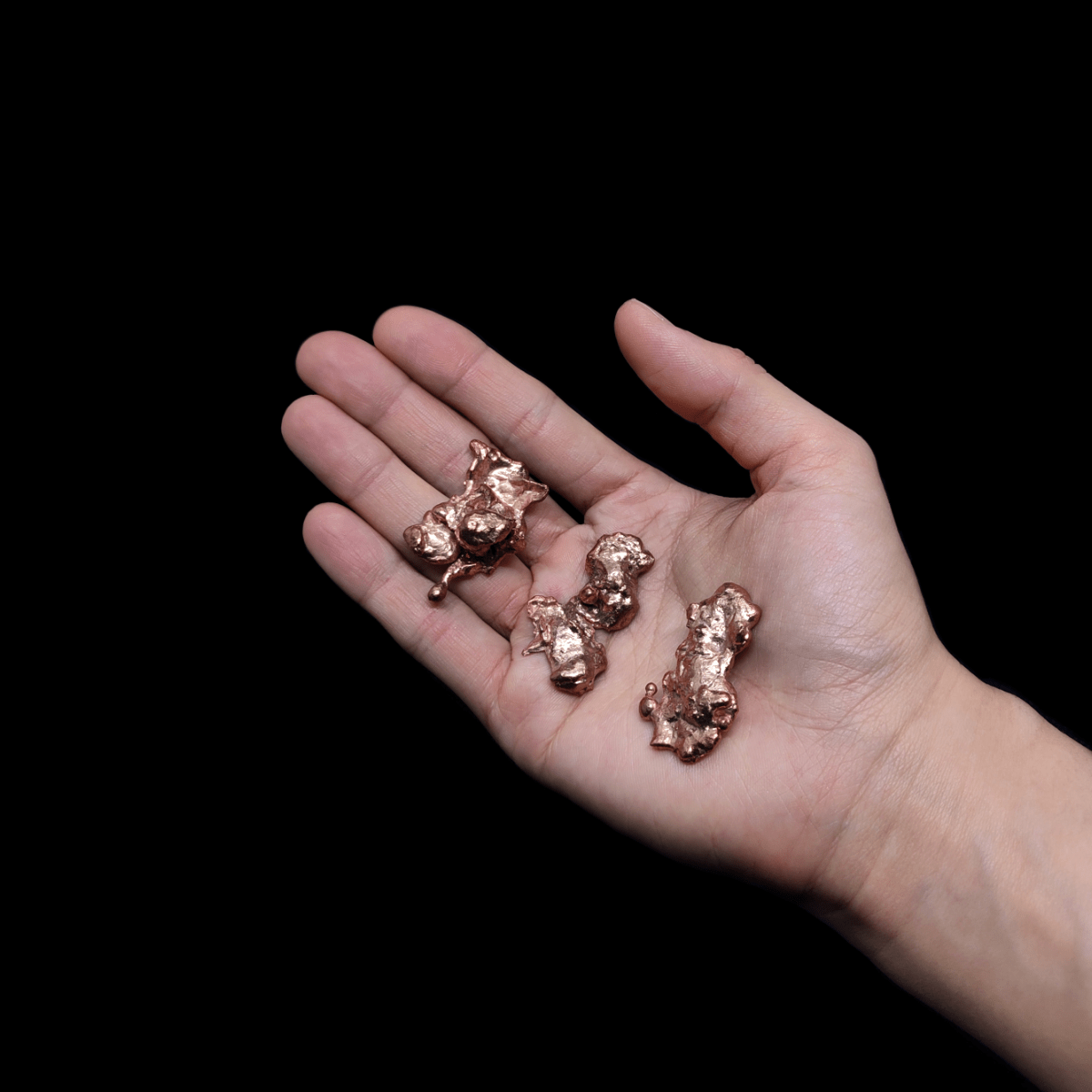 Kleine Kupfer Nuggets welche auf einer Frauenhand liegen.