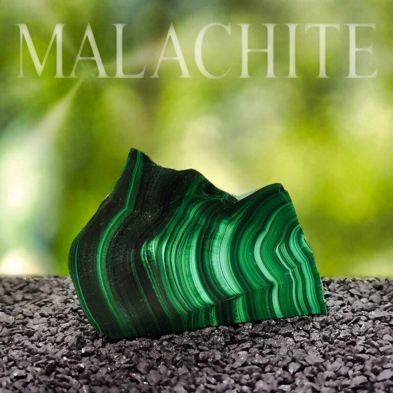 Malachit Edelstein Scheibe auf grünem Lichtungshintergrund. Der Stein steht in schwarzem Kiesbett, über ihm befindet sich ein Schriftzug "MALACHITE".