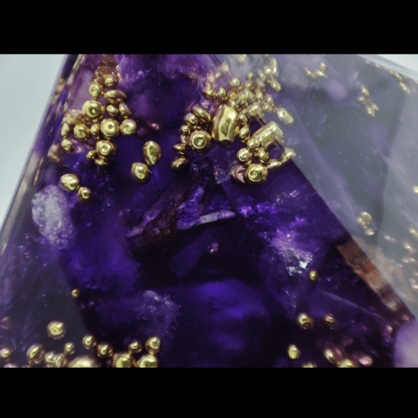 Makro Aufnahme einer violetten Orgonit Pyramide. Zu erkennen ist eine violette Kristallstruktur mit Charoit und glänzenden Messing Perlen.