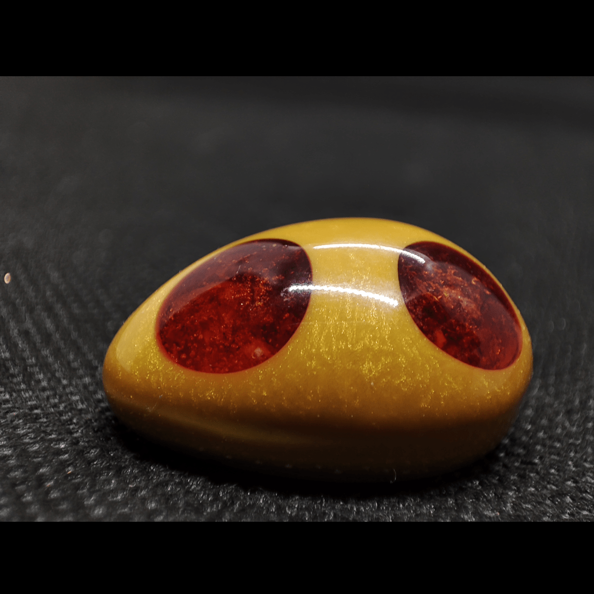 Makro Aufnahme eines goldenen Schmuckstückes mit orangenen Edelsteinpunkten. Es handelt sich dabei um das Orgonit Schmuckstück "Das goldene Ei".