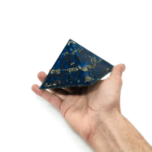 Produktpräsentation einer blauen Orgonit Pyramide, welche aus den Edelsteinen Lapislazuli, Sodalith & Saphir besteht. Zudem sind goldene Metallelemente sichtbar.