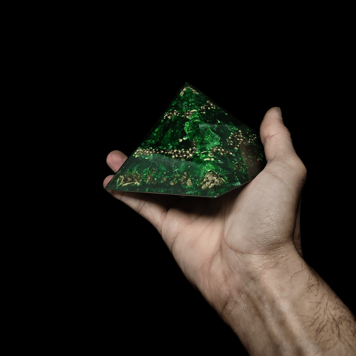 Dunkelgrüne Orgonit Pyramide aus Orgon, Smaragden & Gold, welche von einer Hand gehalten wird.