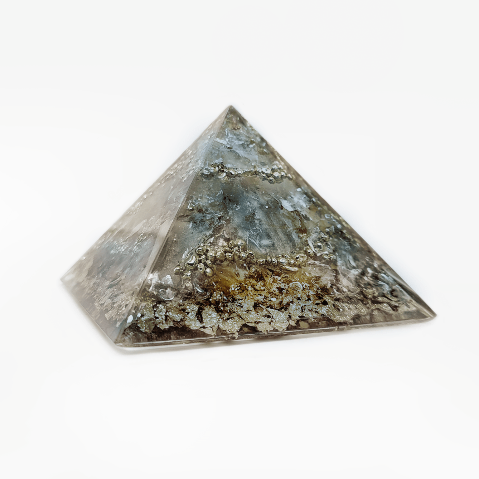 Eine graue, bräunliche Orgonit Pyramide mit silberfarbenen Elementen. Die enthaltenen Edelsteine Rauchquarz, Beiger Quarz & Herkimer Diamant geben diesem Orgon Kunstwerk seine graue Farbe.