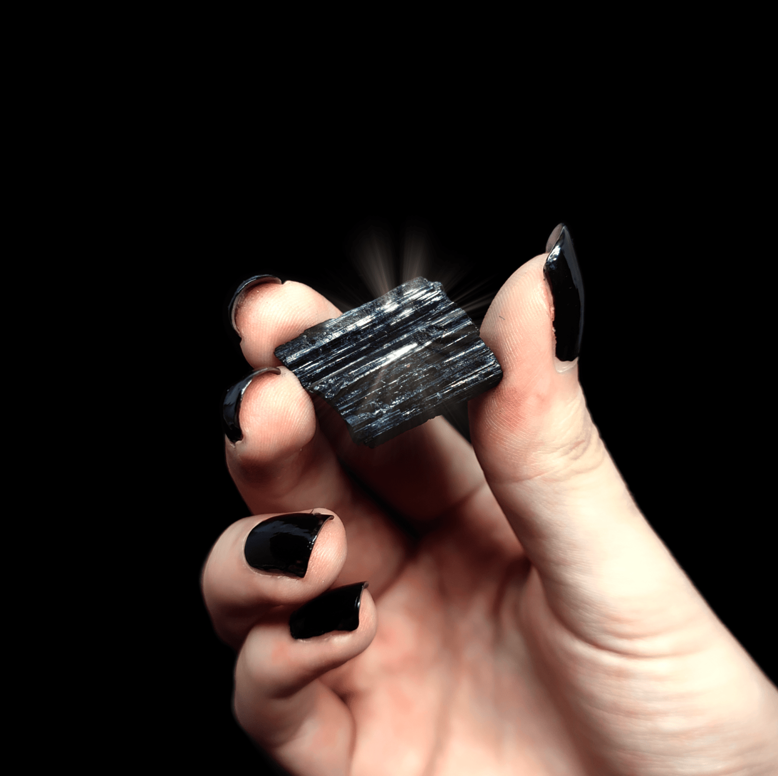 Ein schwarzer Turmalin Kristall mit Beleuchtung, welcher von einer Frauenhand gehalten wird.