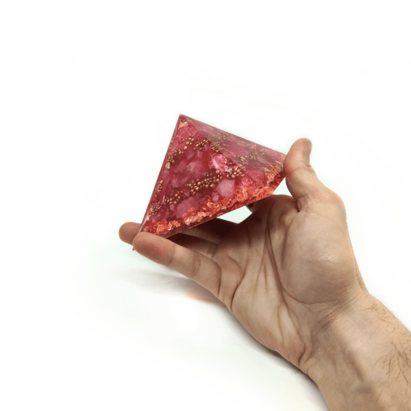 Rosenquarz Pyramide, welche von einer Hand gehalten wird. Dieser Orgonit ist Rosa.