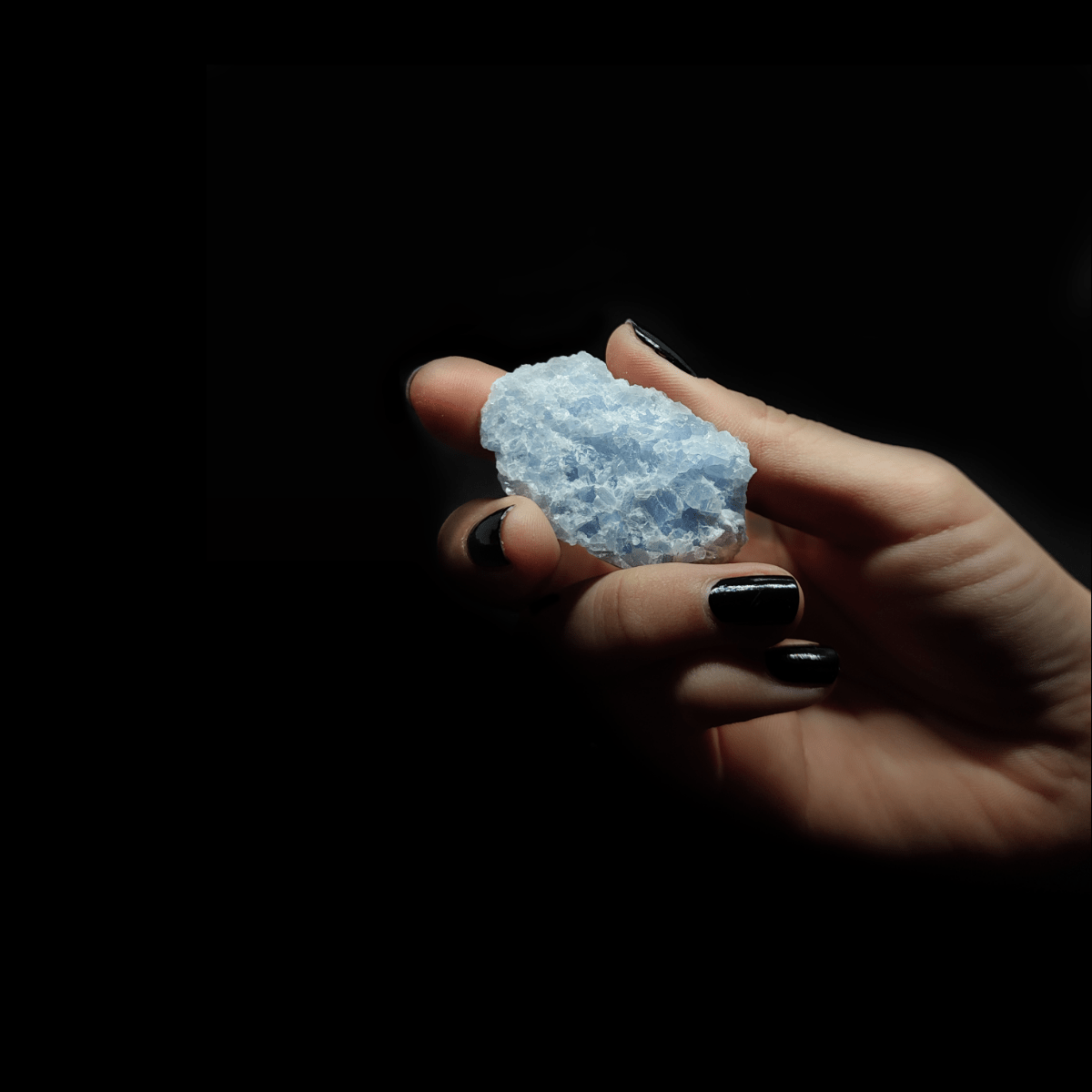 Frauenhand die einen blauen Calcit Rohstein hält. Der Calcit selbst weist eine ausgeprägte Kristallstruktur auf.