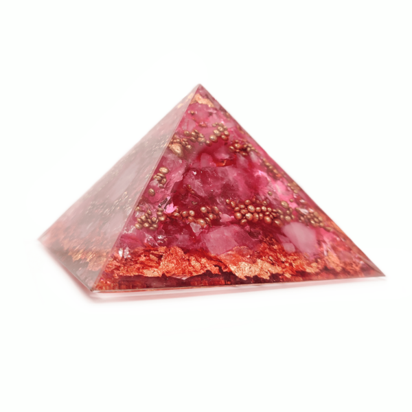 Eine intensiv rosé-farbene Orgonit Pyramide, welche aus Erdbeer & Rosenquarzen besteht. Die Metall Elemente dieses Orgoniten sind in Rosé-goldener Farbe gehalten.