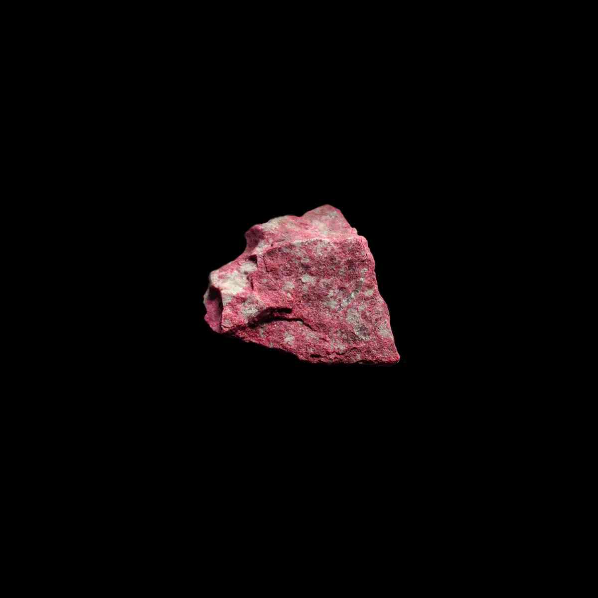 Glänzender Thulit Rohstein auf schwarzem Hintergrund. Thulit ist ein rötlicher Edelstein aus Norwegen & die rote Variation des Minerals "Zoisit".