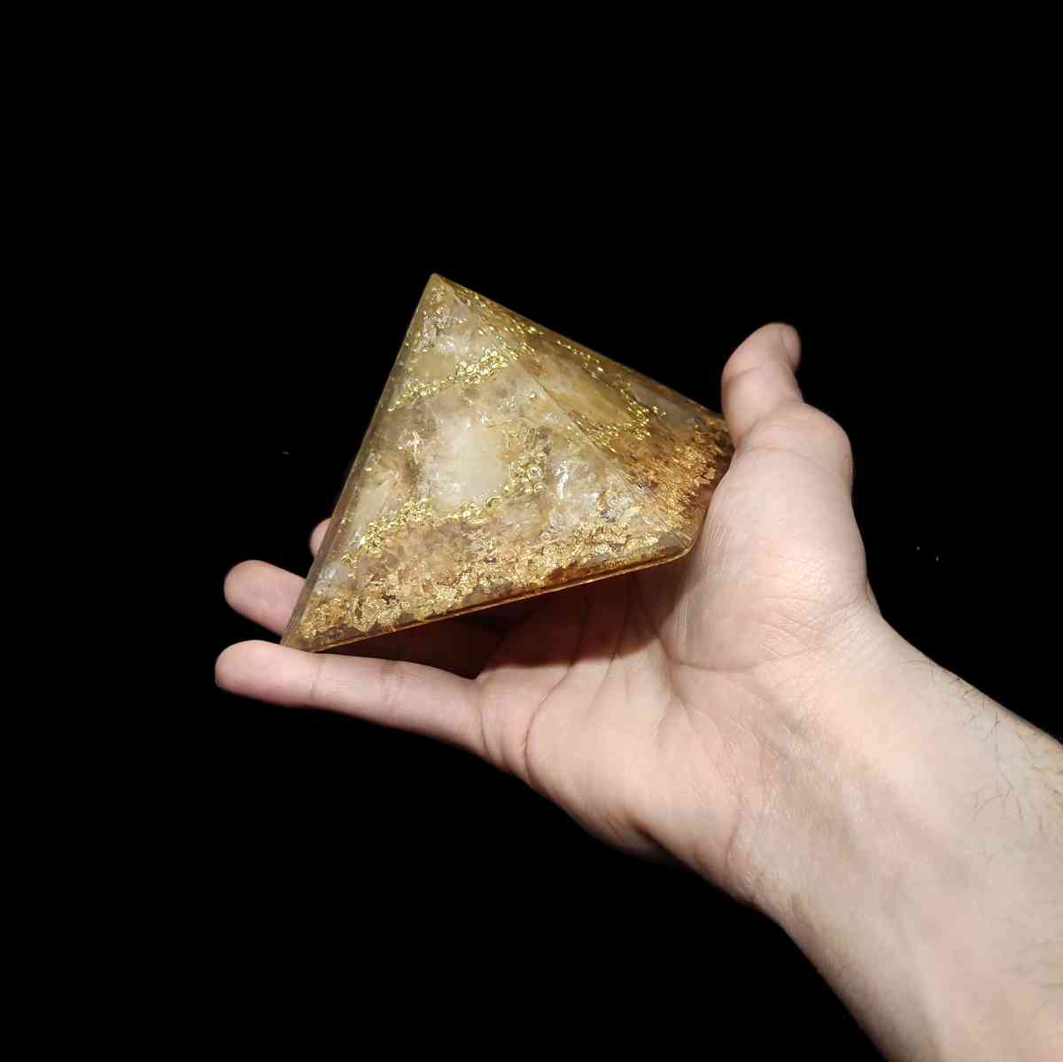 Champagnerfarbene Edelstein Orgonit Pyramide, welche von einer Hand gehalten wird.