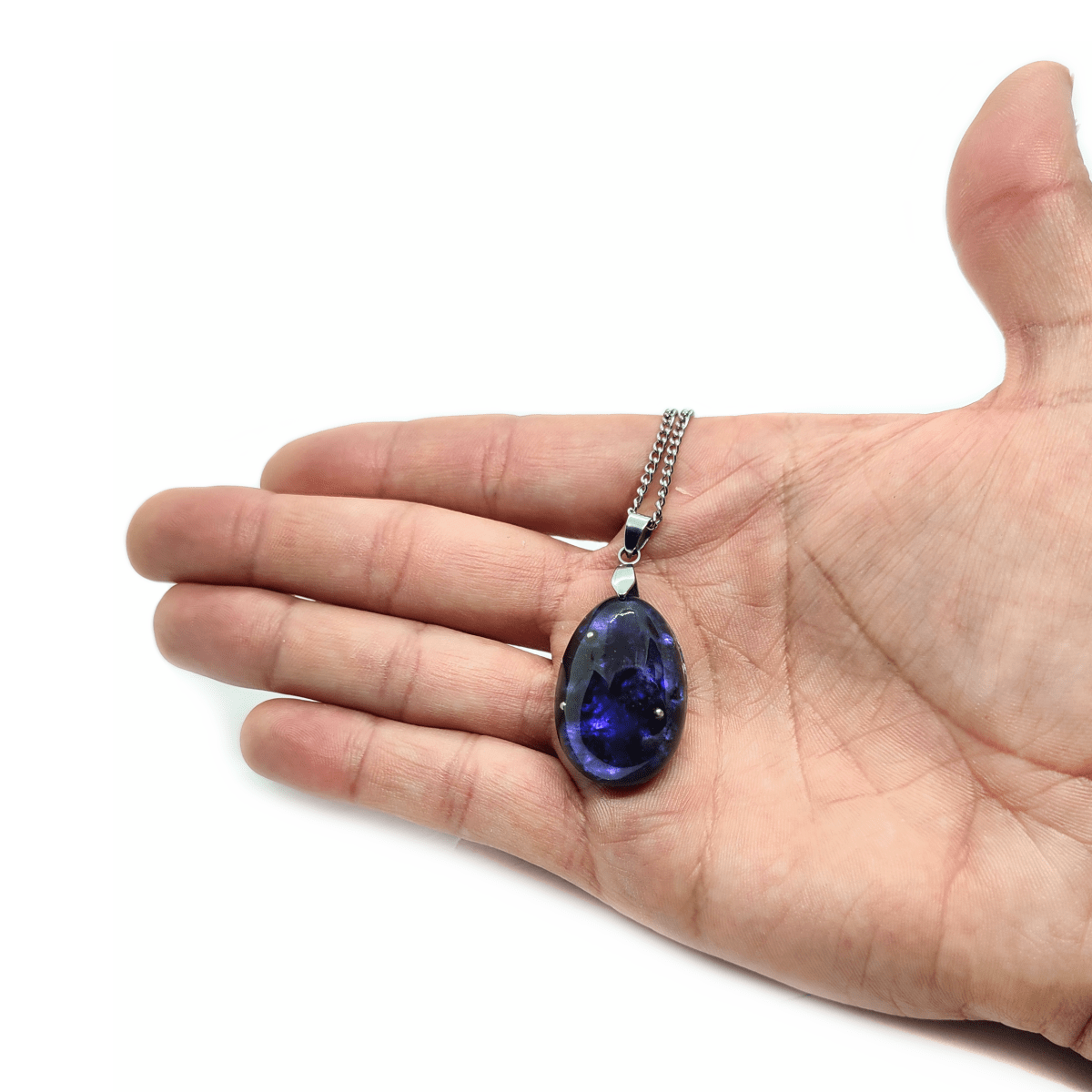 Dunkelblaues Orgonit Amulett mit stark glänzenden Kristallen & silberner Halskette, welches von einer Hand gehalten wird.
