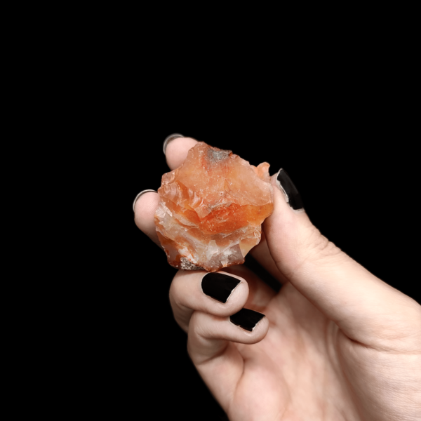 Ein dunkler orangener Karneol Rohstein welcher zur Produktpräsentation von einer Hand gehalten wird.