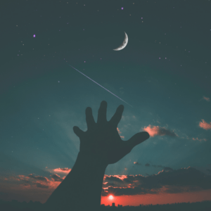 Eine Hand welche zum nächtlichen Himmel in Richtung Mond gestreckt wird.