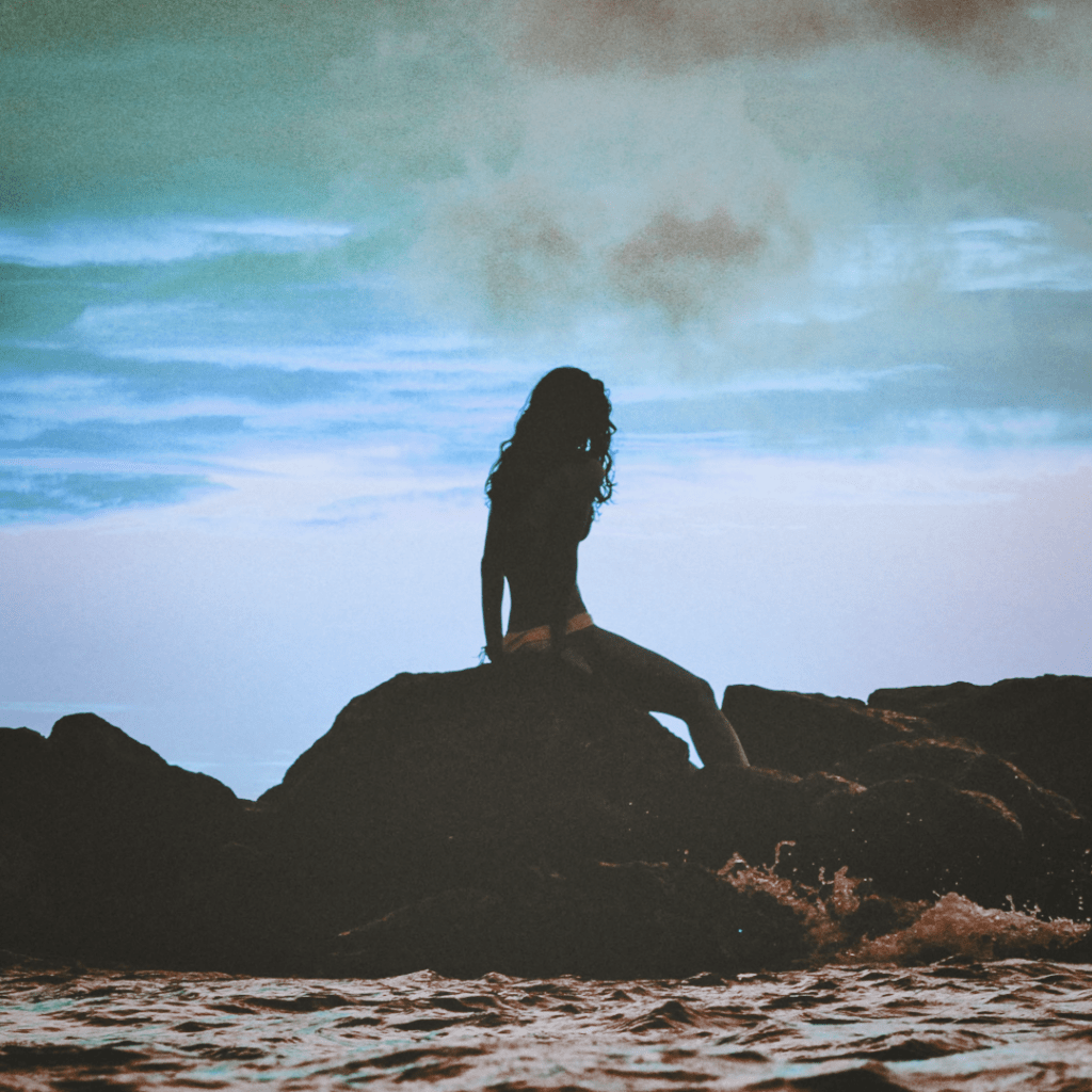 Eine Frau, welche an einer windigen Küste sitzt. Symbolbild für die Bedeutung des Sternzeichens Wassermann.