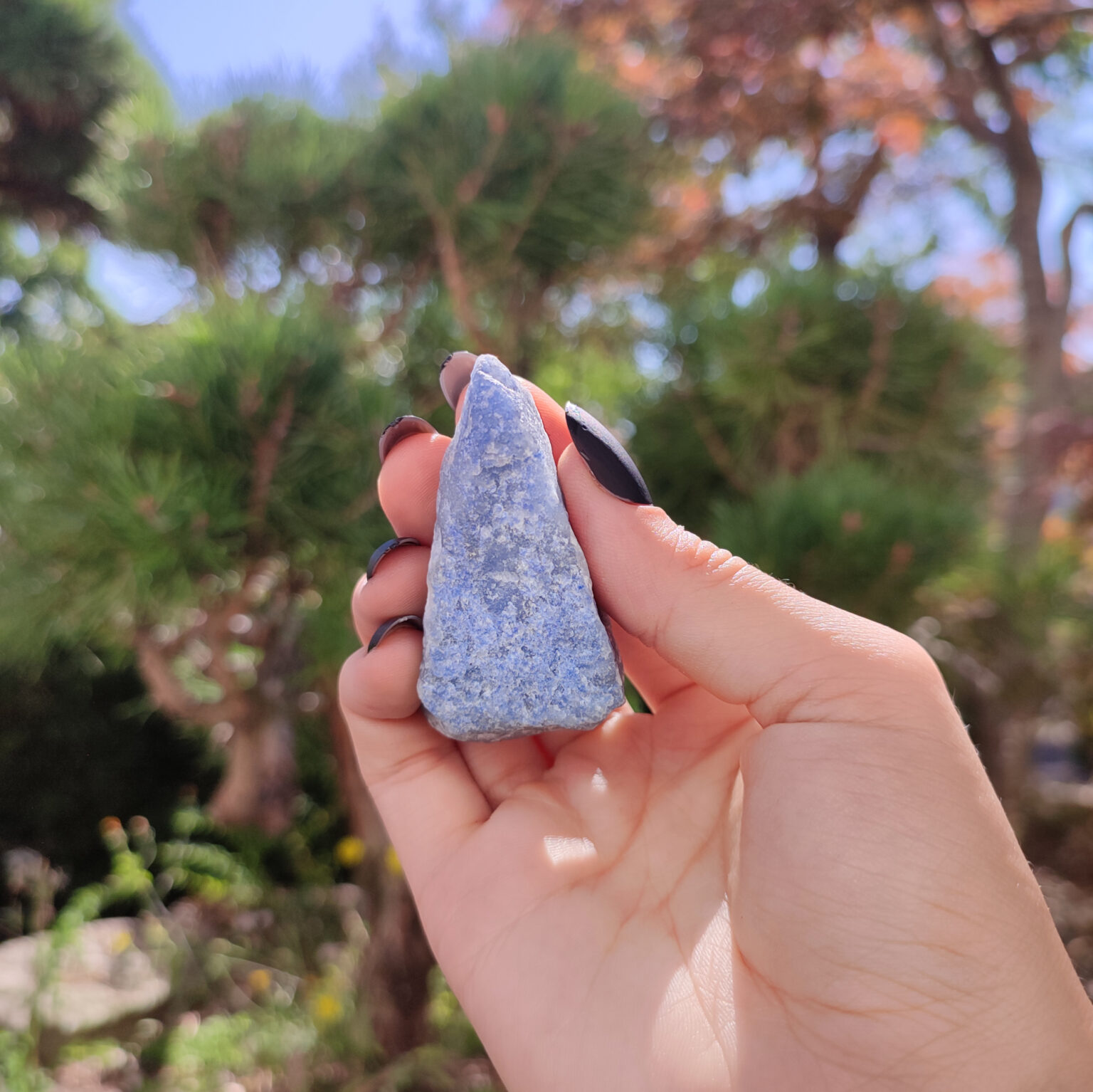 Roher blauer Aventurin Kristall welcher von einer Hand in der Natur gehalten wird.