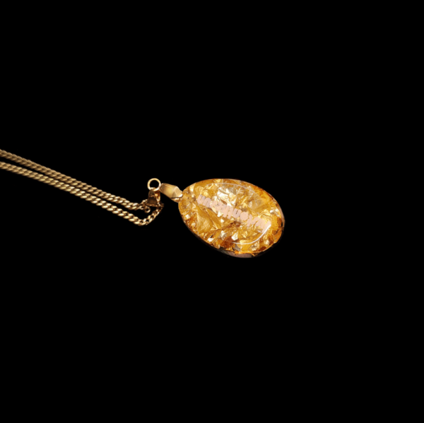 Die Rückseite eines echten Orgonit Anhängers, welche mit Goldflocken bedeckt ist. Das Amulett ist an einer vergoldeten Kette befestigt.