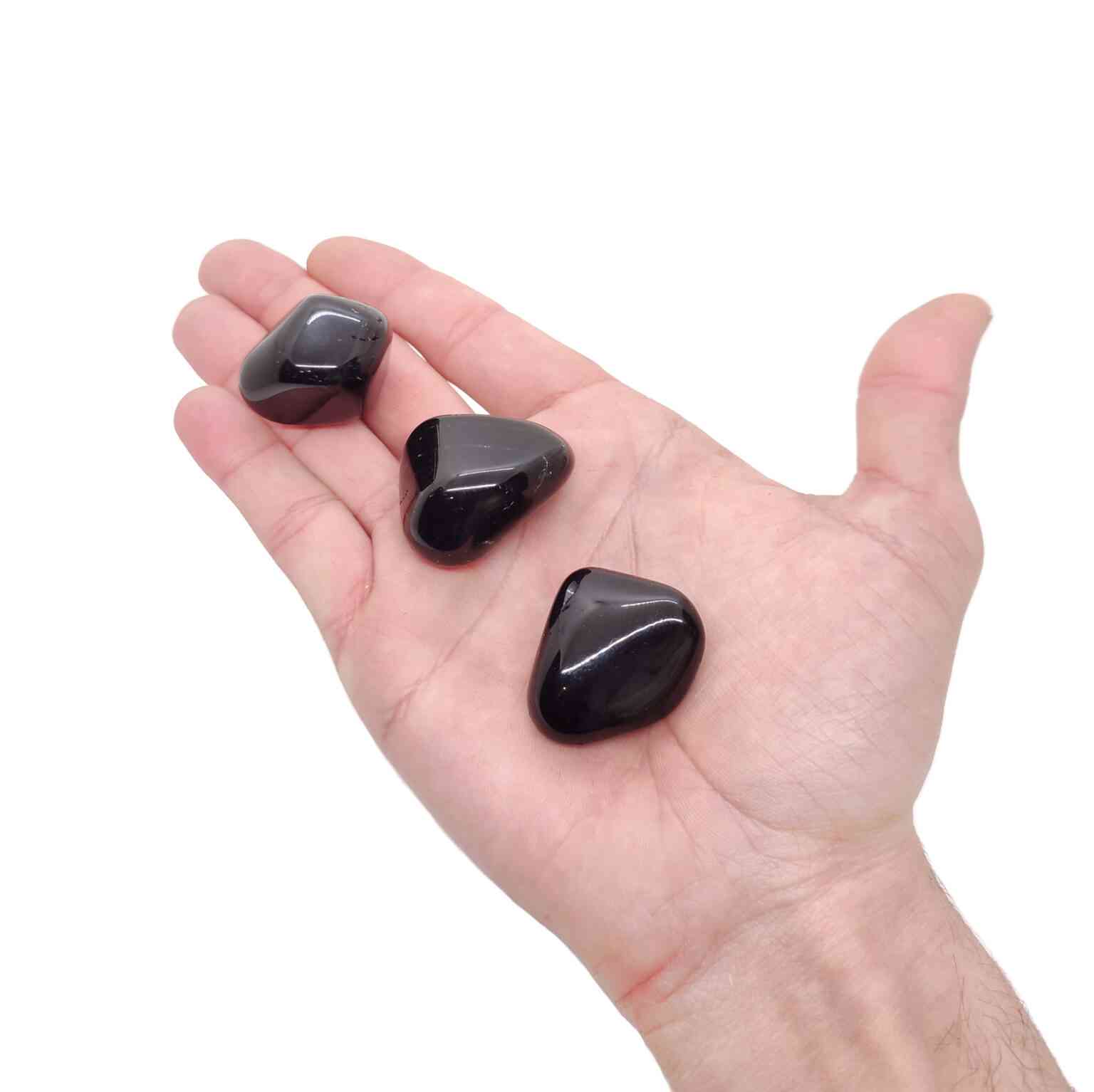 Schwarze Obsidian Trommelsteine auf einer Handfläche.