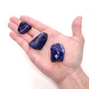 Intensiv blaue Sodalith Trommelsteine auf einer Hand.