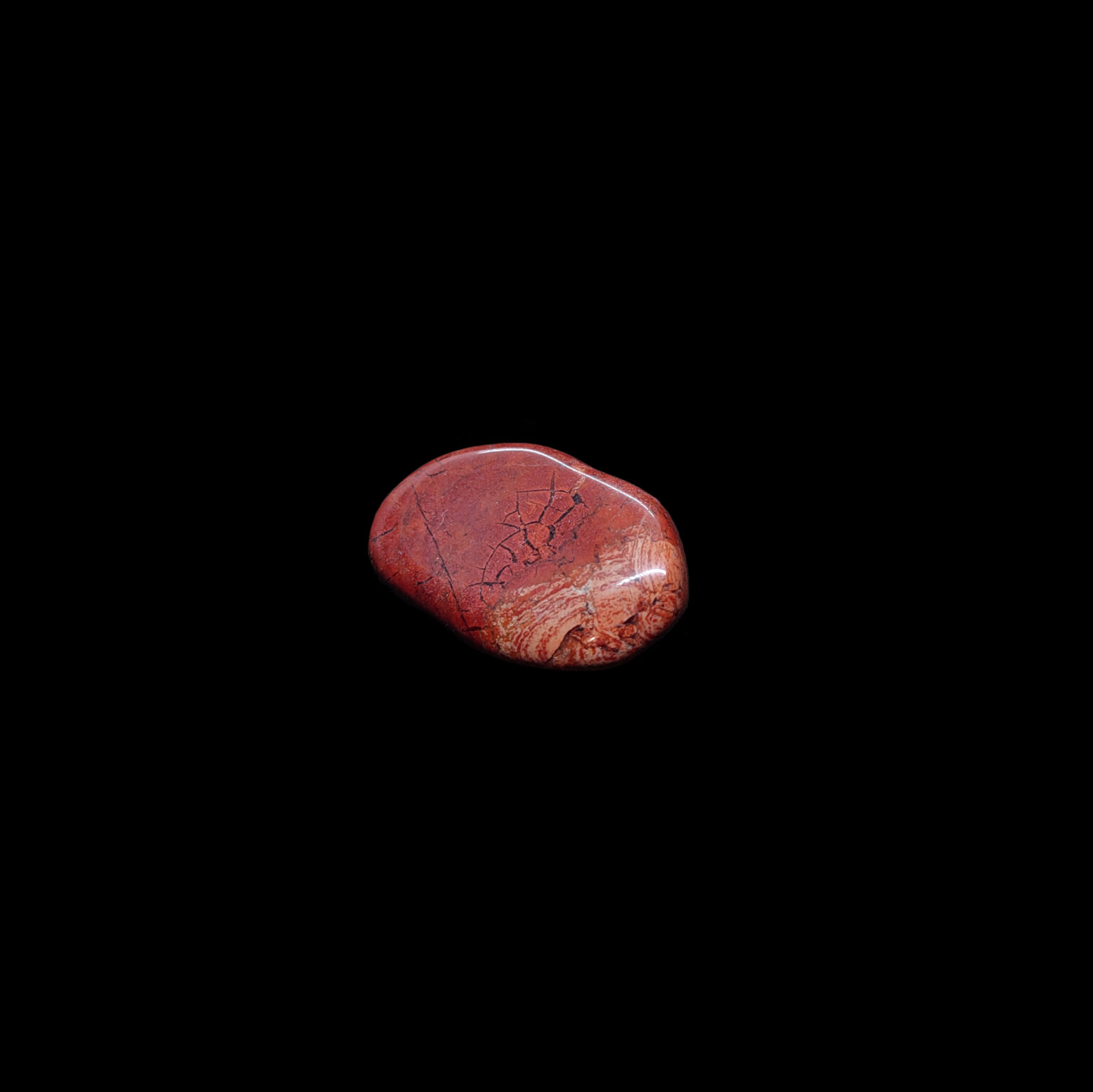 Ein roter Jaspis Trommelstein. Der Jaspis Kristall hat Bänderungen.